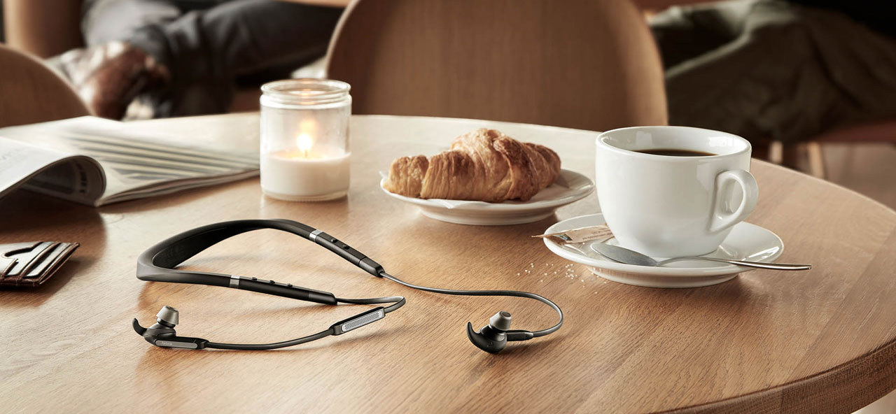 The Jabra Elite 65e on display on a dinner table, with a magazine, a cup of coffee, a plate with bread, and a bottled candle on the table